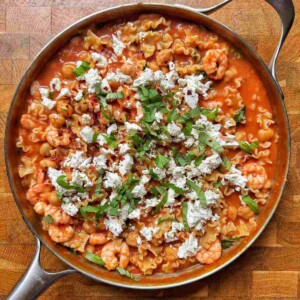 Overhead view of one pot tomato shrimp pasta in a skillet with chickpeas, crumbled feta and fresh basil.