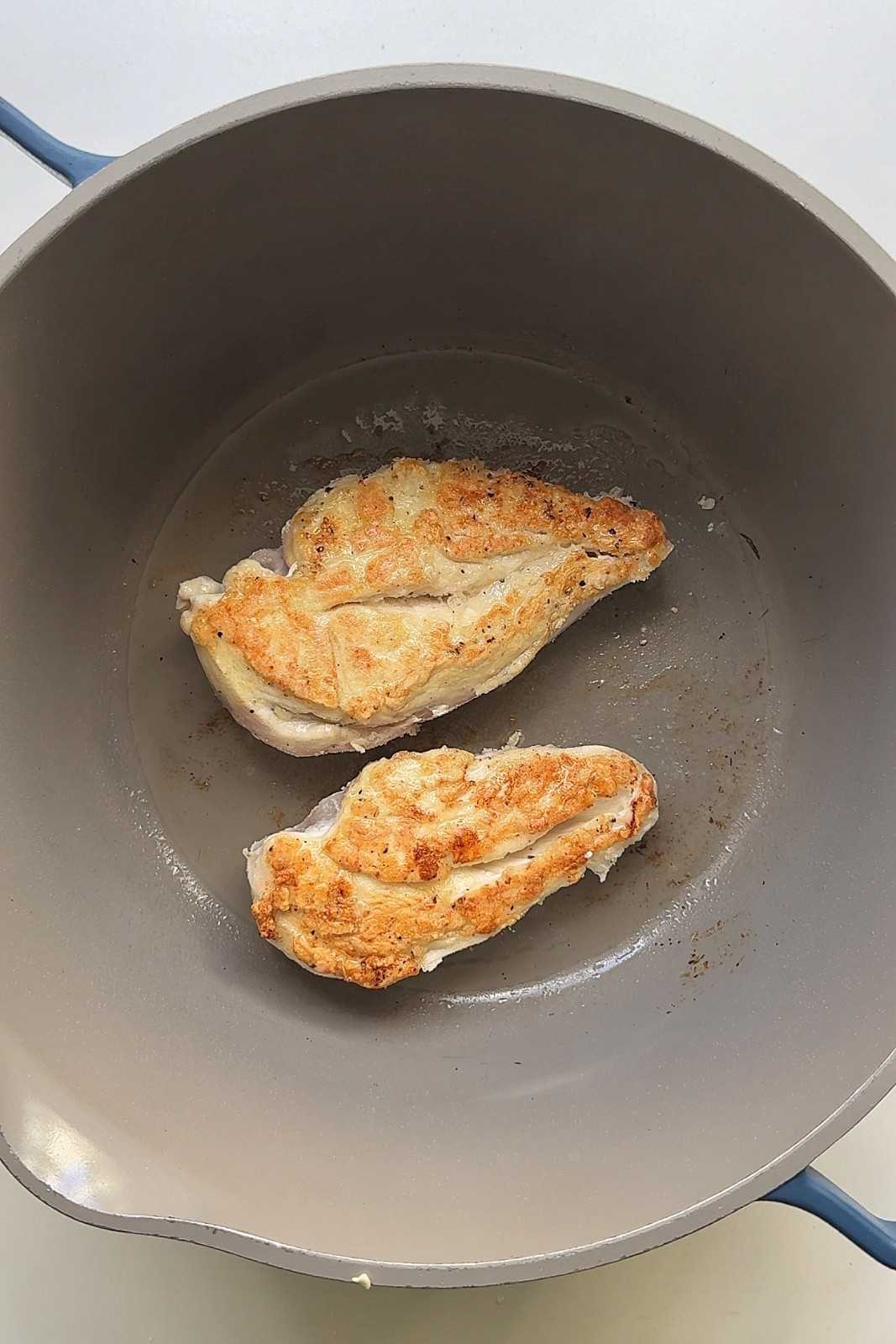 Two flour-coated chicken breasts seared golden brown in a deep gray pan.
