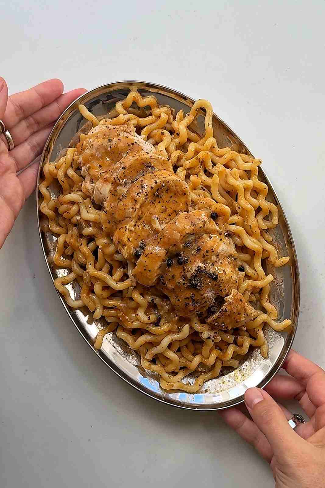 Chicken au poivre pasta on an oval steel platter with sliced chicken breast down the middle and whole peppercorns on top.
