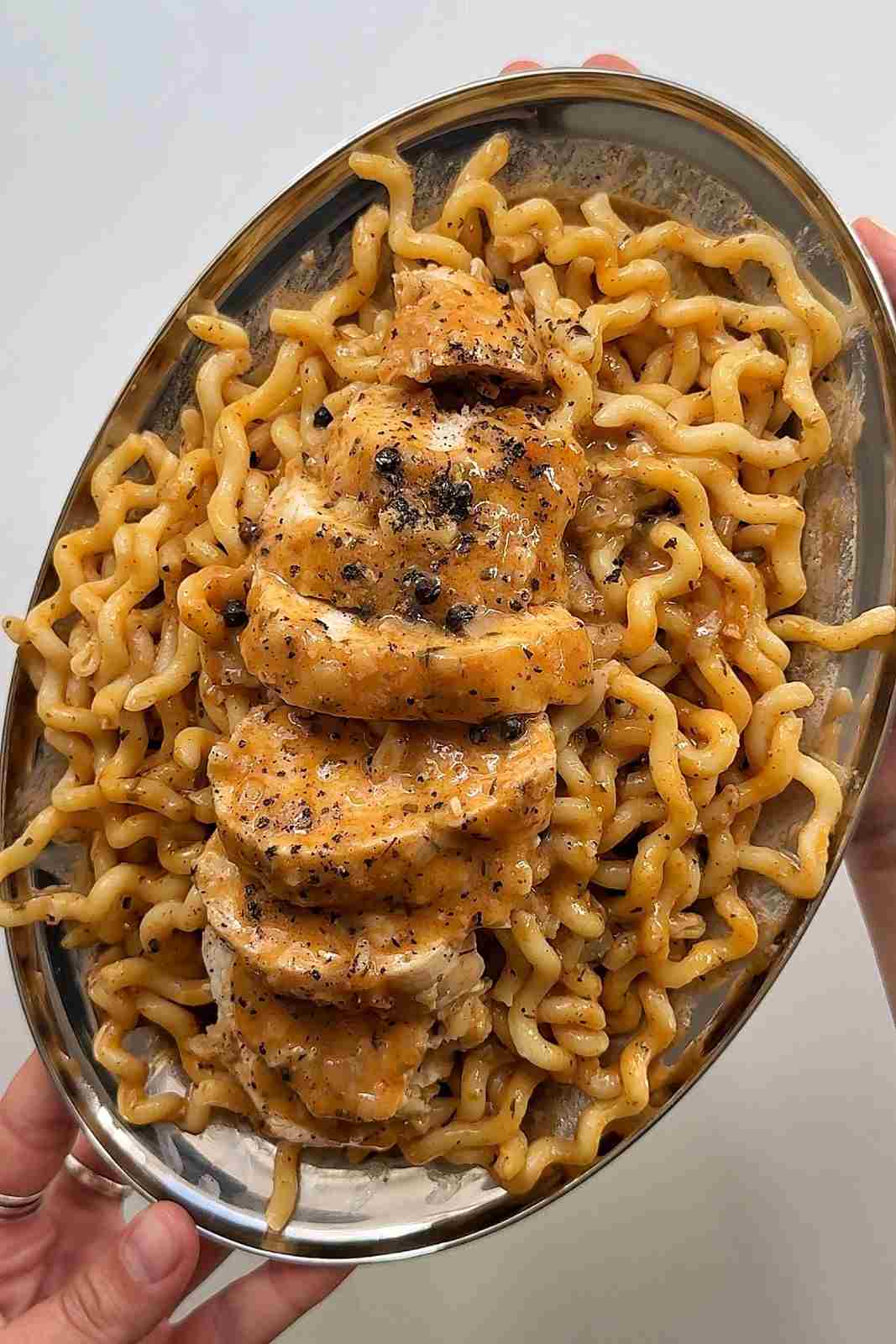 Chicken au poivre pasta on an oval steel platter, with slices of chicken breast in creamy peppercorn sauce over long wavy pasta.