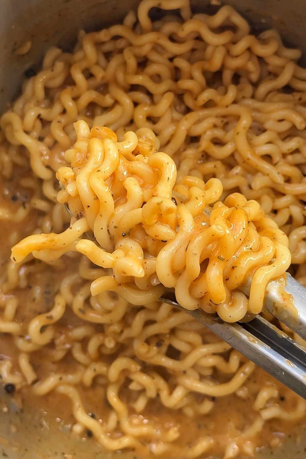 Tongs lifting wavy pasta coated in creamy peppercorn sauce out of the pot.