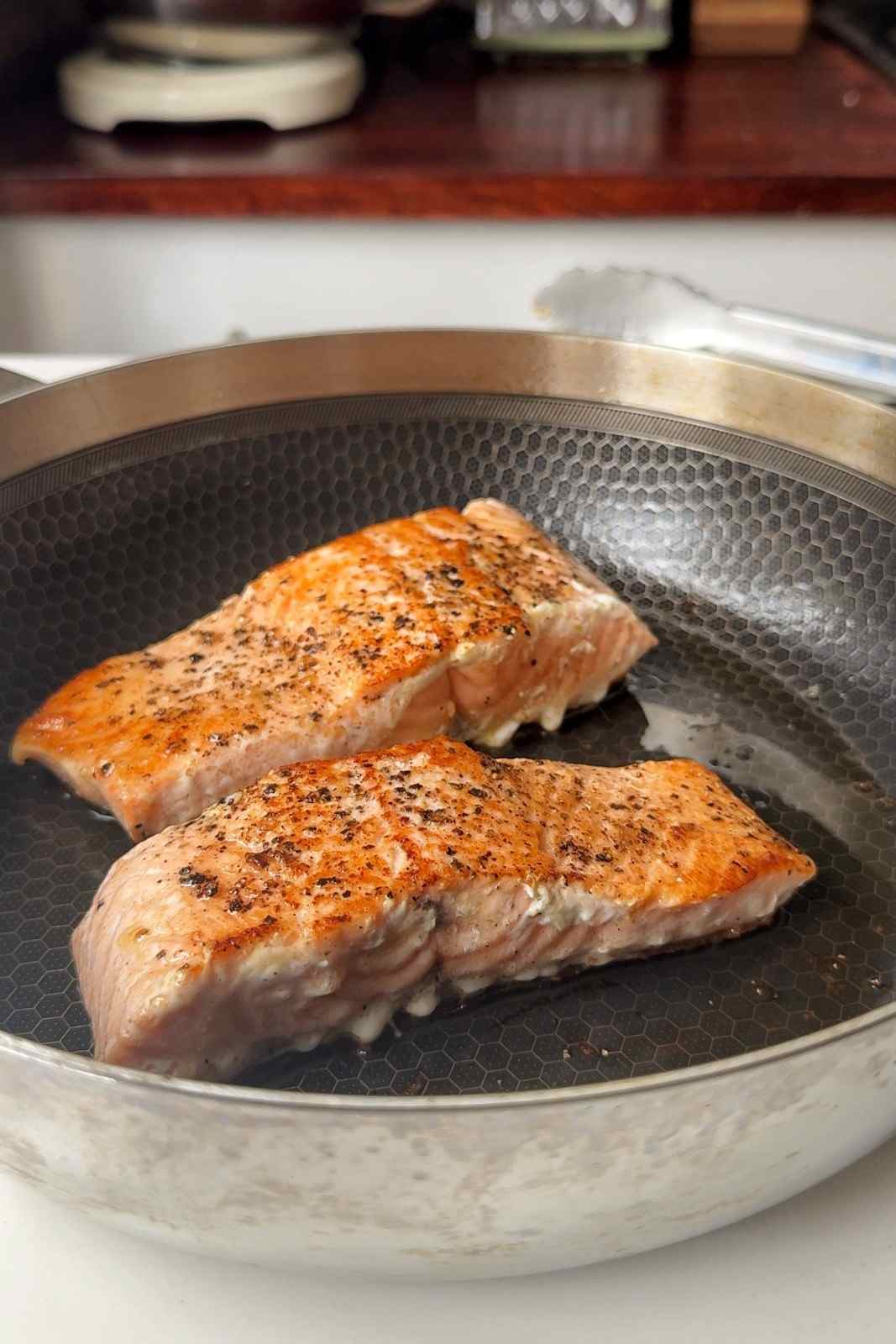 Two salmon fillets seasoned with black pepper, seared golden in a deep skillet for creamy Boursin salmon orzo.