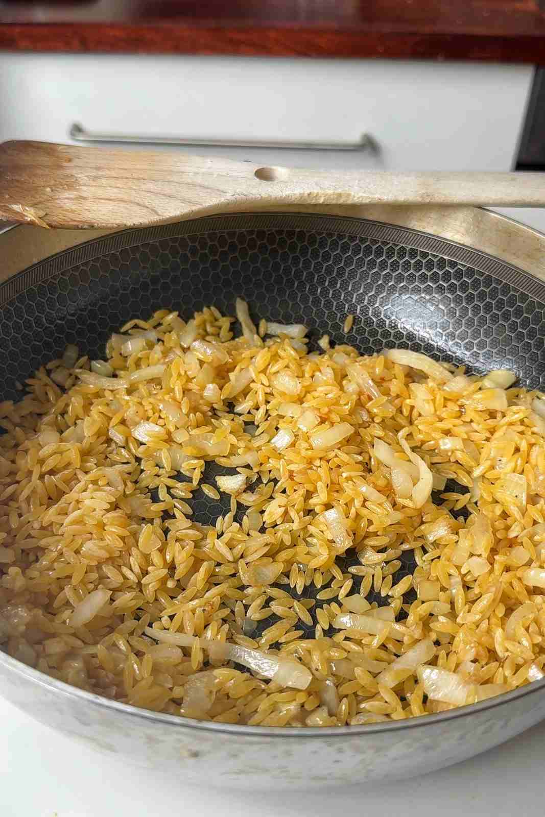 Uncooked orzo stirred through softened onion and garlic in a deep skillet.