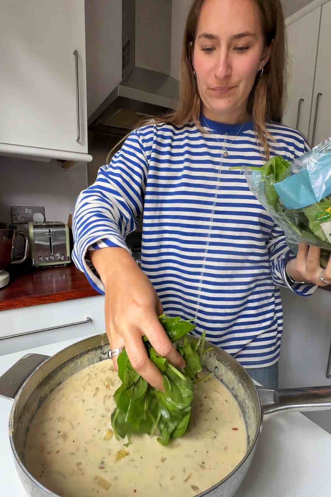 Emily Roz adding a handful of fresh baby spinach to a creamy Boursin orzo sauce.