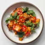Overhead view of creamy halloumi curry over basmati rice on a white plate, topped with fresh cilantro and sliced red chilies.