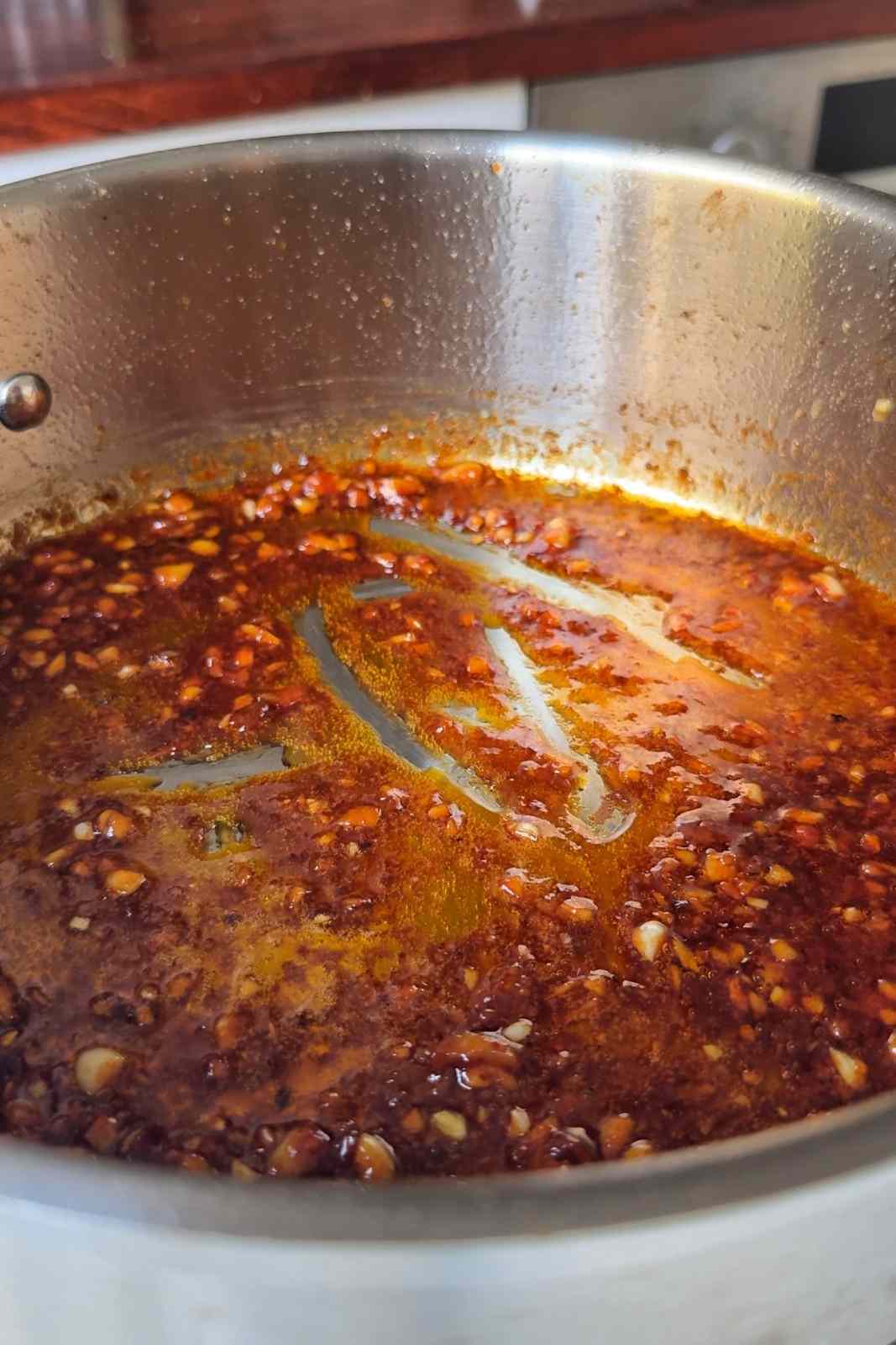 Sriracha, soy sauce and honey bubbling with minced garlic into a glossy red glaze in a stainless steel pan.