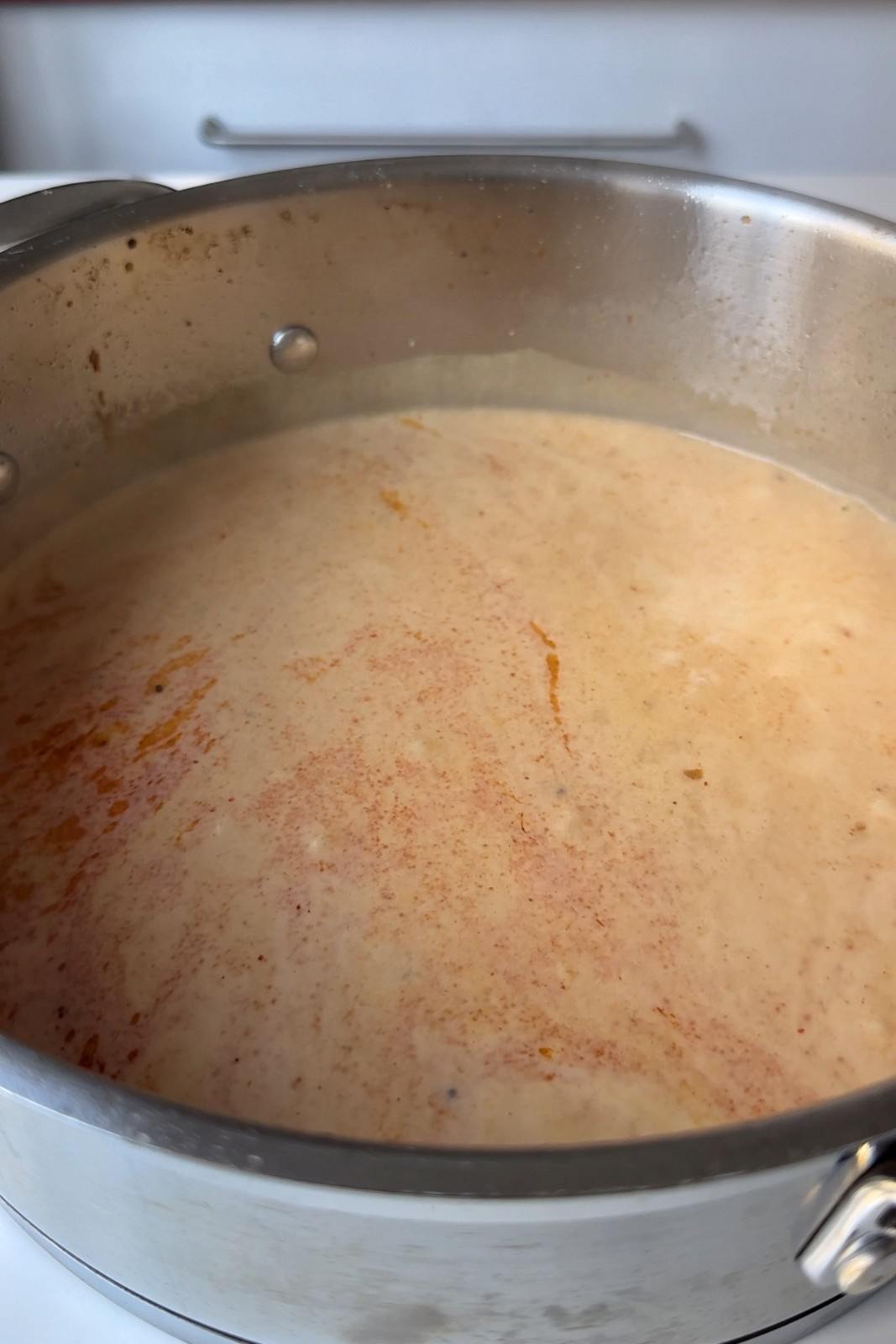 Coconut milk and chicken stock just added to the pan, a pale creamy sauce streaked with orange from the sriracha glaze.