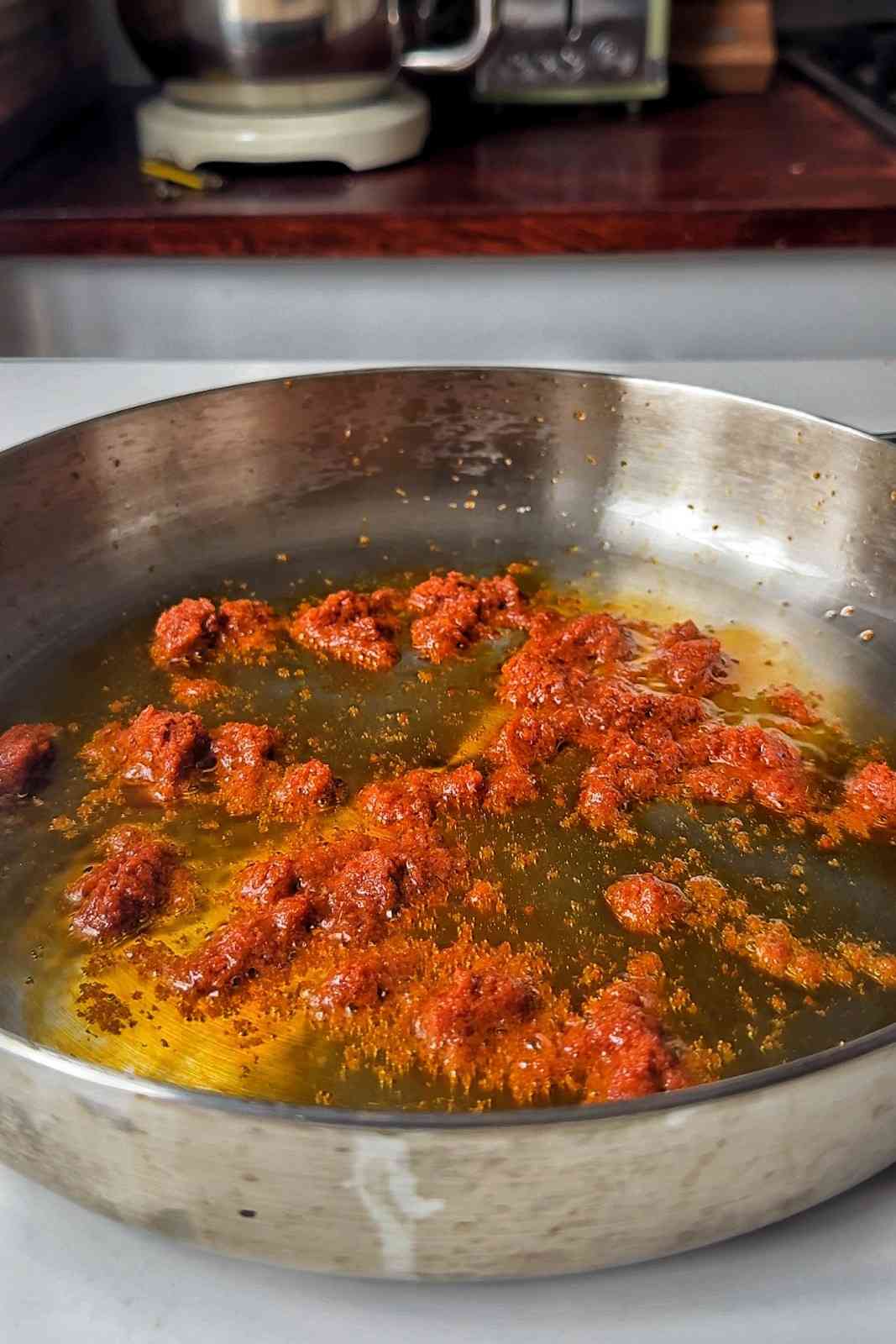 Red curry paste sizzling in vegetable oil in a stainless steel skillet.