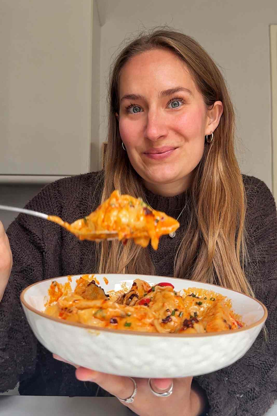 Emily Roz holding a bowl of satay sauce dumplings and lifting a spoonful toward the camera.