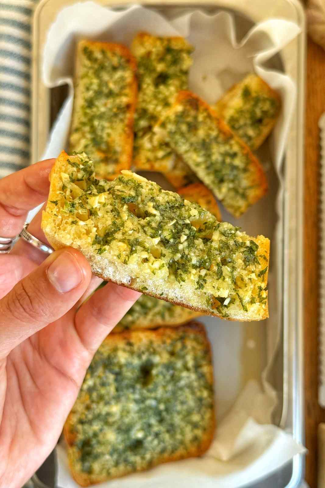 Emily Roz holding a piece of her ciabatta garlic bread with parsley and parmesan, sliced on a board.