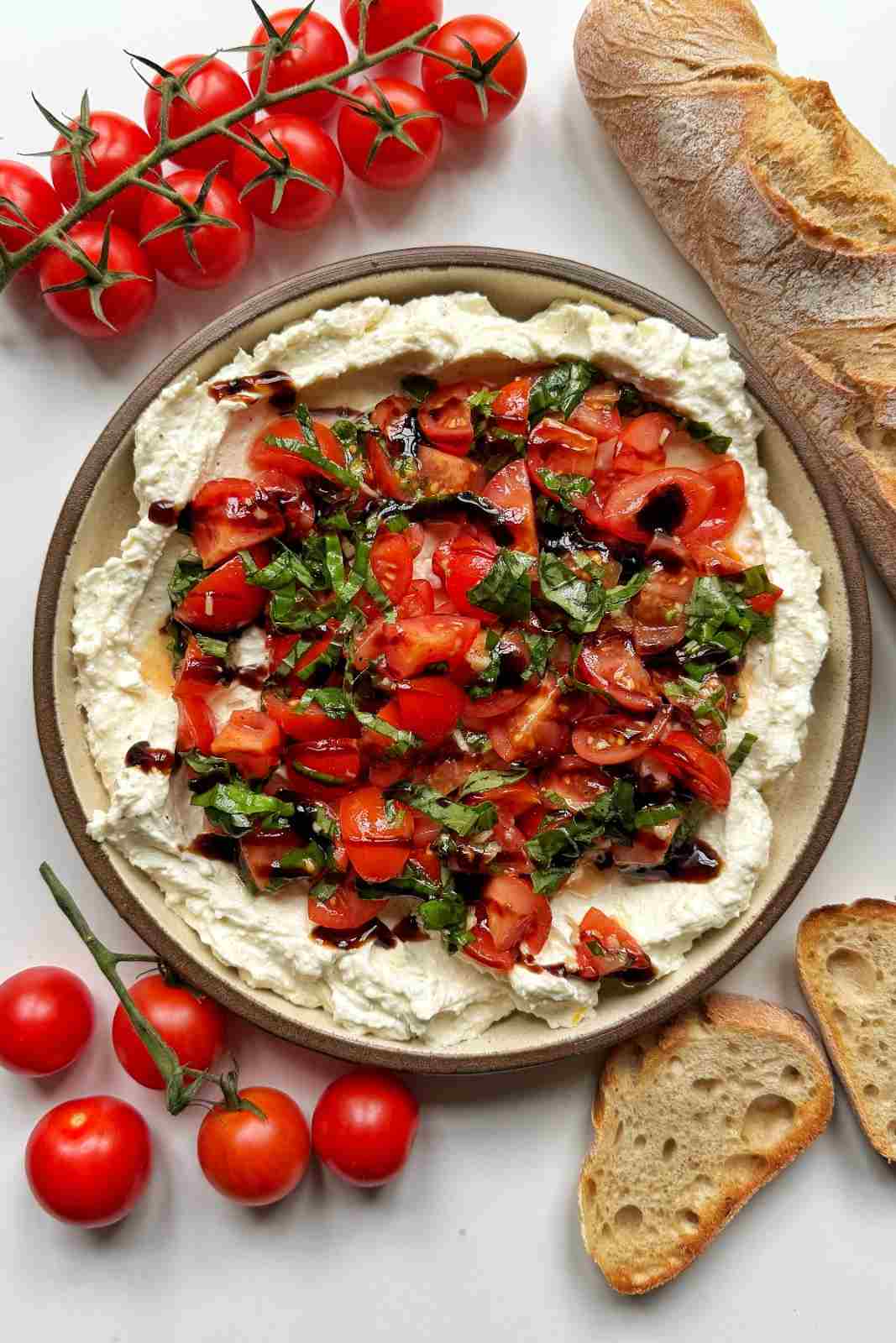 Whipped cream cheese and feta bruschetta dip topped with garlicky cherry tomatoes and basil.