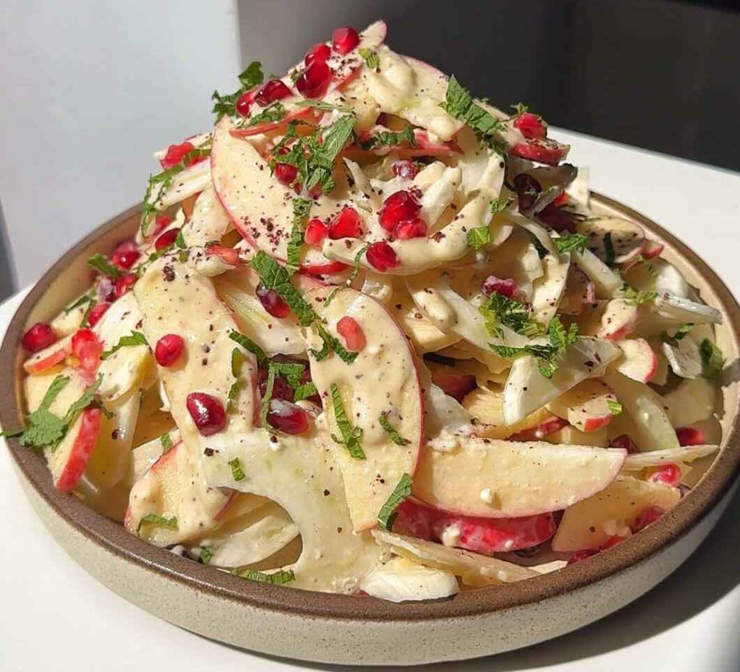 A serving of apple fennel salad, topped with mint and pomegranate seeds.