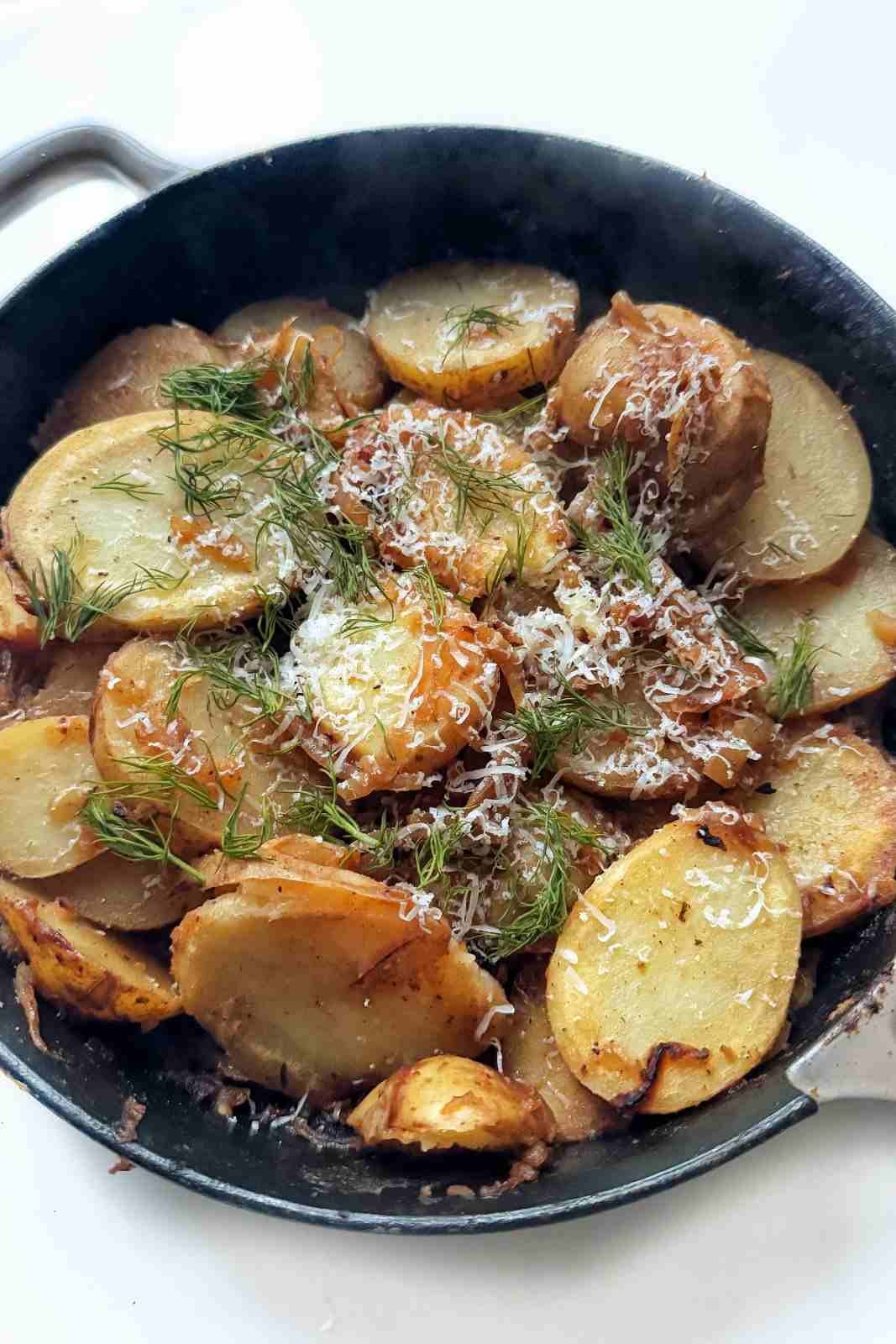 A skillet full of fried potatoes and onions topped with parmesan and chives.