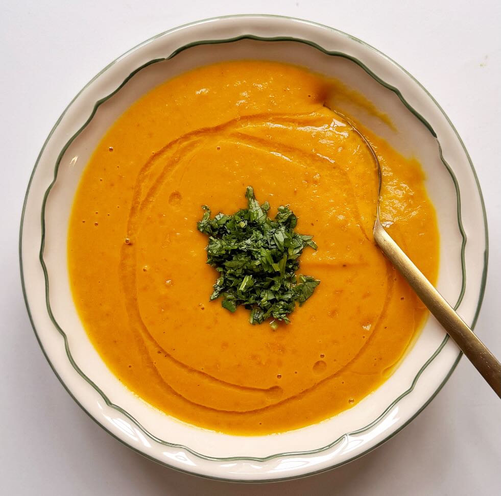 A bowl of carrot ginger soup made using carrots, sweet potato, ginger, garlic, coconut milk, and a handful of other ingredients.