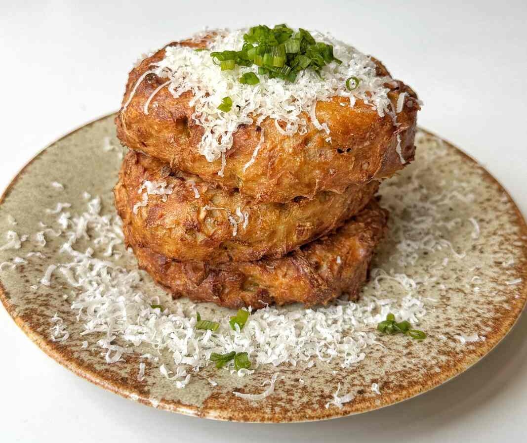 Three crispy air fryer hash browns stacked on a plate, topped with parmesan.